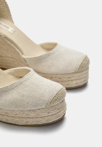 Beige lærred wedge espadrilles med rund tå og tekstureret jute platform. Glat stofoverdel, flettet jute-detalje rundt om sålen.