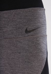 Legginsy sportowe Nike w szarym kolorze, charakteryzujące się gładką teksturą, czarnym logo oraz kontrastowym czarnym pasem w talii.