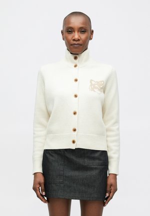 Cream-colored cardigan with a high collar, button front, and a knitted fox design on the chest. Features ribbed cuffs and hem.