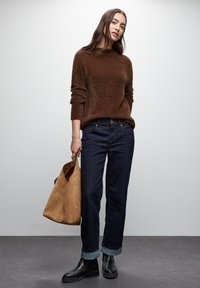 Brązowy futrzany sweter, ciemnoniebieskie dżinsy z podwiniętymi mankietami, czarne botki za kostkę oraz torebka zamszowa w kolorze tan. Prosty design, casualowy wygląd.