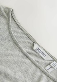 Hellgraues ärmelloses Oberteil aus weichem, strukturiertem Stoff mit weitem Ausschnitt. Das Etikett zeigt Größen- und Markendetails.