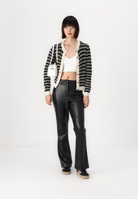 Zwart-wit gestreepte cardigan met knopen, gecombineerd met zwarte leren flared broeken en zwarte sneakers met beige zolen. Witte handtas.