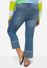 Jeans de mezclilla azules claros de campana con dobladillos deshilachados, que cuentan con dos bolsillos traseros y una cintura de tiro medio, combinados con una sandalia plana.