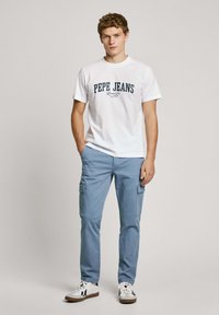 White cotton t-shirt with "PEPE JEANS" graphic in navy, paired with light blue cargo pants featuring side pockets and white sneakers.