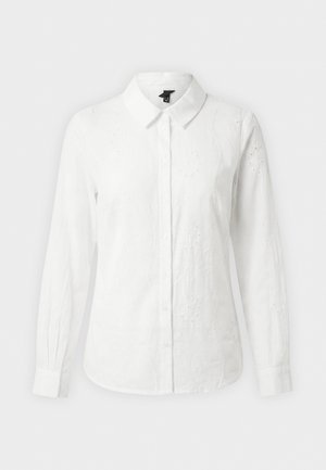 Valge pikkade varrukatega nööbitav pluus kraega, õrna lillemustrilise tikandiga ja vormitud mansettidega ühtlasel taustal.