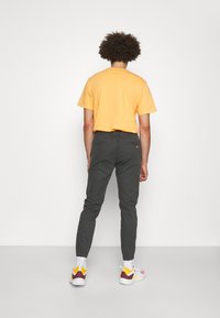 Oranje katoenen t-shirt met een fitted snit. Grijze taps toelopende broek met elastische tailleband en twee achterzakken. Kleurrijke sneakers met contrasterende accenten.