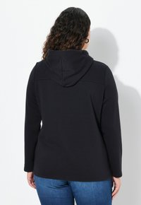 Zwarte hoodie met lange mouwen, voorzien van een capuchon en een gladde, zachte textuur. Het ontwerp heeft een simpele, strakke snit met een relaxte pasvorm.