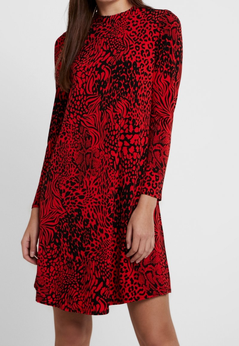 Robe rouge arborant un mélange de motifs léopard et abstraits en noir. Encolure ronde, manches longues et coupe décontractée jusqu'aux hanches.