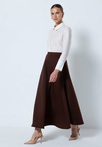 Brown A-line skirt paired with a white long-sleeve button-up shirt. The outfit is complemented by nude heeled shoes. Smooth textures and classic design.