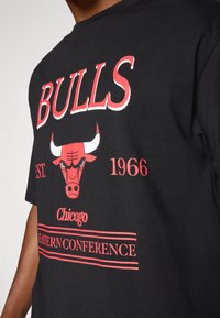 Sort bomulds T-shirt med fed rød "BULLS" tekst, et Chicago Bulls-logo samt detaljer som "EST. 1966" og "EASTERN CONFERENCE" tekst.