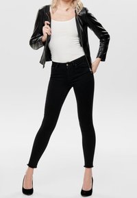 Jean skinny noir taille haute, associé à un débardeur blanc ajusté et un blouson en cuir noir court. Chaussures à talons noirs.