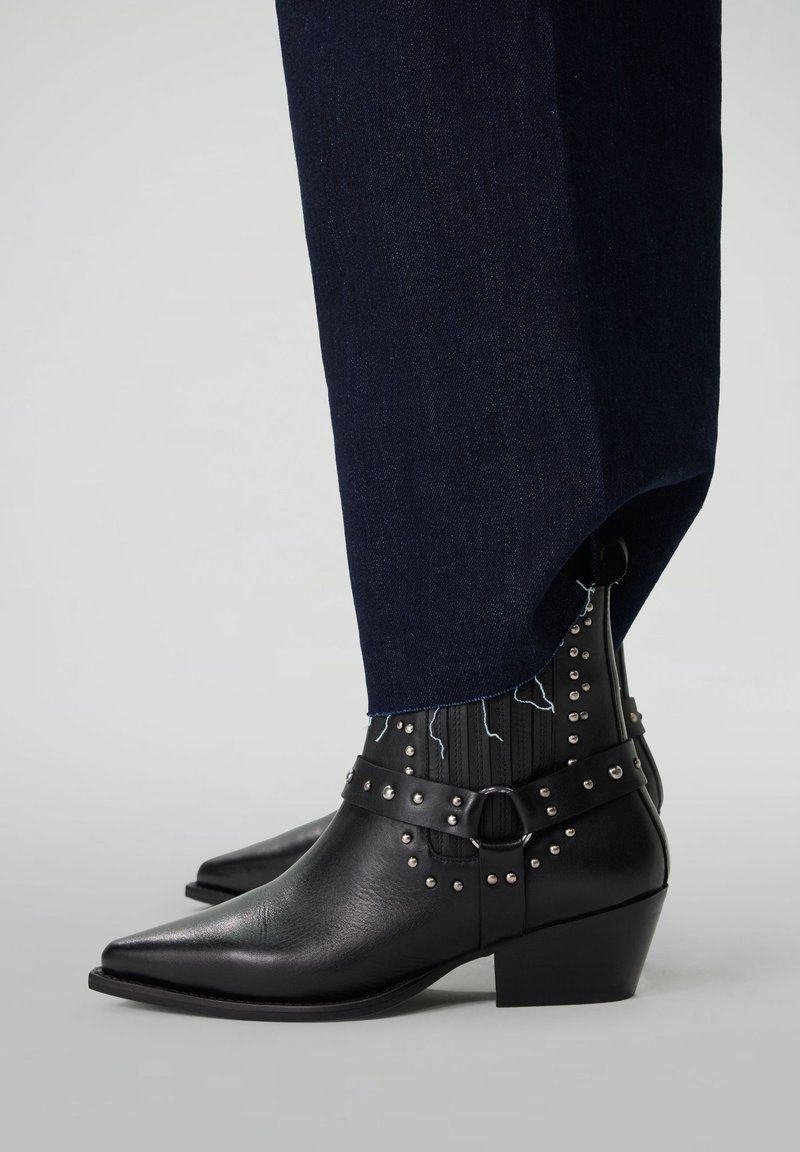 Zwarte leren enkelboots met puntige neuzen, gestepte accenten en chunky hakken, gecombineerd met donkere denim broek met een rafelige zoom.