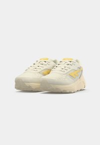 Light-colored athletic shoes featuring a textured suede and mesh upper, yellow accents, and a thick, patterned rubber sole.