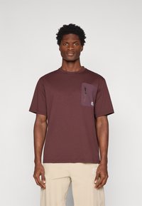 T-shirt a maniche corte color bordeaux con taschino chiuso da zip sul petto, scollo rotondo e vestibilità comoda. Realizzato in tessuto morbido e liscio.