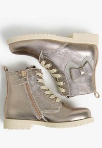 Bottines métalliques rose gold avec une surface texturée, lacets crème, fermeture éclair sur le côté et un accent en nœud sur le talon. Semelle en caoutchouc.