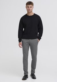 Must mustriga, mis on paaritatud heledate hallide, kohandatud pükstega. Riietusel on klassikaline ümar kaelus ja tekstuuriga kanga detailid. Mustad jalatsid lõpetavad ilme.