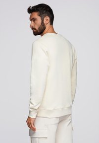 Cremefarvet sweatshirt med lange ærmer, ribbede manchetter og kant; blød tekstur. Bæres med matchende lysfarvede cargo-bukser.