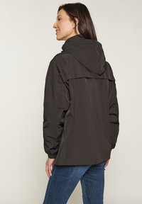 Schwarze Kapuzenjacke aus leichtem Material, mit elastischen Bündchen, einem Rückenbelüftungsfach und einem lockeren Schnitt, kombiniert mit Jeans.