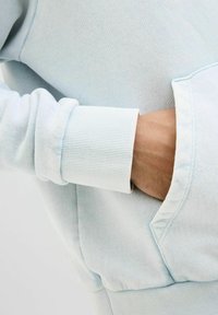 Light blue sweatshirt featuring ribbed cuffs and a front pocket, made from soft, textured fabric with a subtle pattern.