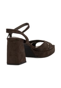 Sandalias de tacón alto de ante marrón con un amplio tacón cuadrado, correas entrelazadas y diseño abierto en los dedos. Suela plana negra, textura suave.