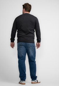 Pulover tricotat gri închis, blugi bleu din denim și adidași albi casual. Detalii vizibile de cusătură pe spate și detalii ale buzunarelor pe blugi.