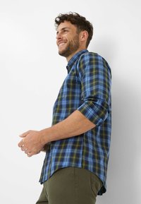 Blau- und grünkariertes Hemd mit hochgeschlagenen Ärmeln, knöpfbarem Kragen und abgerundetem Saum. Leichter Stoff mit glatter Textur.