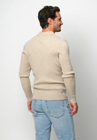 Beige geripptes Sweatshirt mit rundem Halsausschnitt, figurbetontem Schnitt und langen Ärmeln, kombiniert mit hellblauen Jeans.