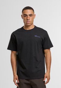 Černé bavlněné tričko s krátkými rukávy a kulatým výstřihem, s modrými textovými akcenty na hrudi. Hladký materiál, volný střih.