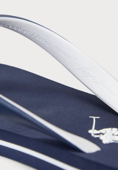 Navy flip-flops with white straps, featuring textured fabric and a silver logo. Strap inscribed with a design quote.