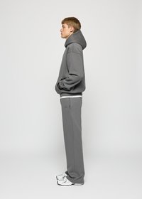 Grey sweatshirt and matching sweatpants, made of soft fabric. Features a hood, front pocket, and embroidered logo on the leg. Worn with white sneakers.