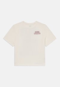 Lys beige kortermet T-skjorte laget av myk bomull, med et lite rosa grafikk som leser "Squishmallows" på venstre bryst.
