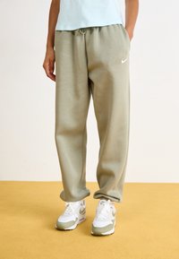 Světle zelené bavlněné tepláky s elastickým pasem, bočními kapsami a malým bílým logem Nike na levém stehně. Nosí se s bílými teniskami.