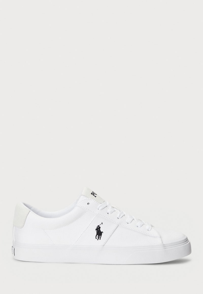 Vita canvas sneakers med platt sula, rund tå och snörningsdesign. Har svart logotyp detaljer på sidan och mjuk strukturerad hälfinish.