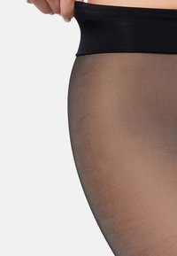 Gennemsigtige sorte strømpebukser med en bred elastik, der har en glat текстur og en transparent finish, som viser en farvegradient.