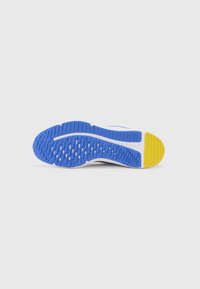 La suola della scarpa sportiva presenta un materiale gommoso blu e giallo, strutturato con scanalature e pattern per una migliore aderenza. La parte intermedia bianca accentua il design.