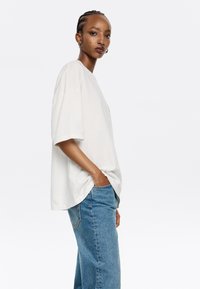 Camiseta de algodón blanca de gran tamaño con mangas cortas, cuello redondo y corte relajado, combinada con unos vaqueros de denim azul de tiro alto.