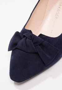 Chaussure plate en daim bleu marine à bout pointu, ornée d'un nœud en tissu sur le devant et dotée d'une doublure intérieure beige.