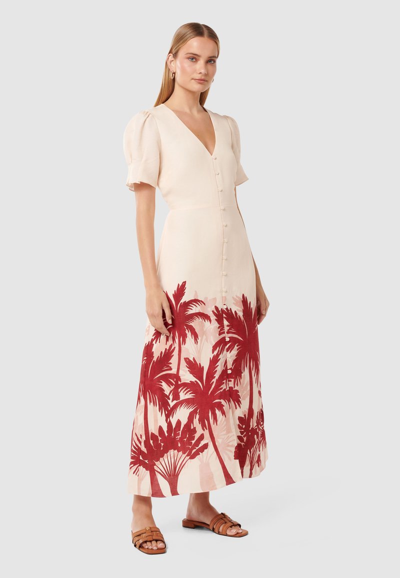 Lichtbeige linnen jurk met een V-hals, korte pofmouwen, knoopsluiting aan de voorkant en een rode palmbomenprint aan de onderkant. Sandalen maken de look compleet.