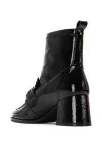 Botín de charol negro hasta el tobillo con punta redondeada, tacón cuadrado y detalle decorativo de correa. Textura suave con un acabado brillante.