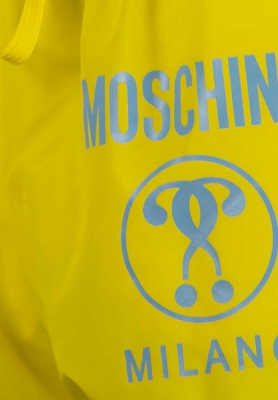 Tissu jaune avec texte Moschino Milano en bleu clair et un logo circulaire présentant deux formes stylisées entrelacées.