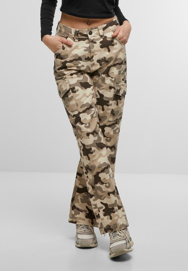 Pantalones cargo caqui con un patrón de camuflaje en varios tonos de beige y marrón. Incluyen múltiples bolsillos y un ajuste relajado.