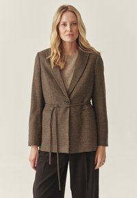 Rjav houndstooth blazer s prilagodljivim krojem, z enim gumbom in ujemajočim pasom, stiliziran čez bež pulover.