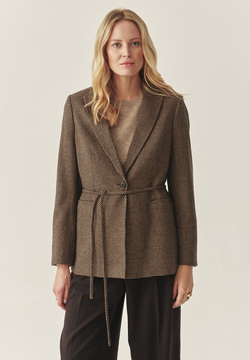 Rjav houndstooth blazer s prilagodljivim krojem, z enim gumbom in ujemajočim pasom, stiliziran čez bež pulover.