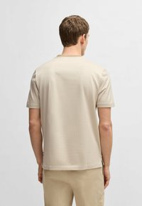 Chemise beige à manches courtes avec un tissu texturé, coupe décontractée et un petit détail de couture au dos. Associée à un pantalon de couleur claire.