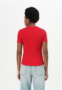 T-shirt rouge ajusté à manches courtes, col rond et texture lisse, porté avec un jean taille haute bleu clair, vu de dos.