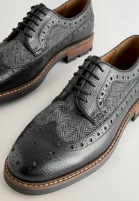 Black leather dress shoes with a herringbone fabric overlay, perforated accents, and a low-profile brown rubber sole. Lace-up design.
