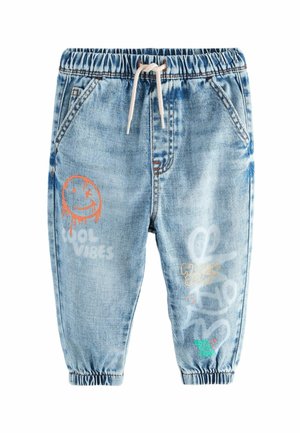 Pantalon jogger en denim bleu clair avec taille et poignets élastiques, cordon blanc et imprimés graphiques colorés incluant un smiley qui fait un clin d'œil et du texte.