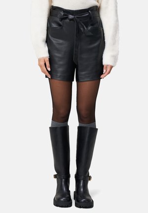 Zwarte leren shorts met een hoge taille, een strikdetail aan de voorkant en twee zakken. Gecombineerd met grijze kniekousen en hoge zwarte laarzen.