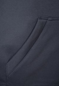 Tela de sudadera azul marino con un bolsillo delantero, acabado liso y texturizado, y costuras reforzadas a lo largo de los bordes.