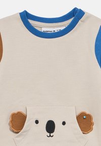 Μπεζ και μπλε παιδικό πουκάμισο με πρόσωπο κοάλα και καστανά αυτιά που προεξέχουν από την μπροστινή τσέπη, ριμπ μπλε γιακά και μανίκια με χρωματικό μπλοκ.